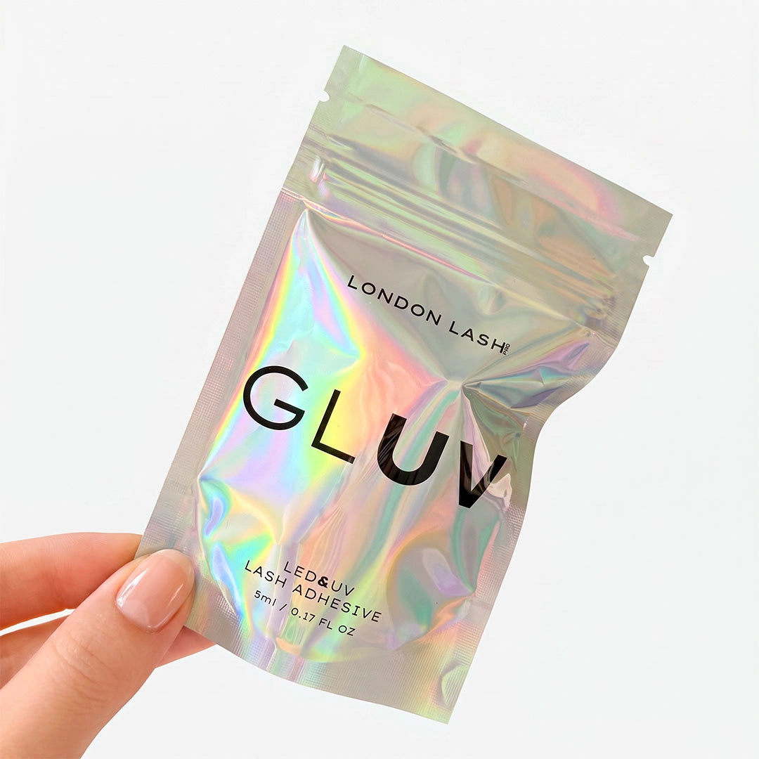 Une main tenant le sachet refermable holographique irisé de la colle pour extensions de cils London Lash GLUV LED & UV.